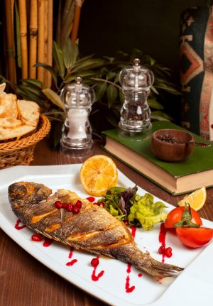 grilled-whole-fish-with-yellow-sauce-vegetable-salad-lemon-pomegranate-seeds-white-plate_114579-263
